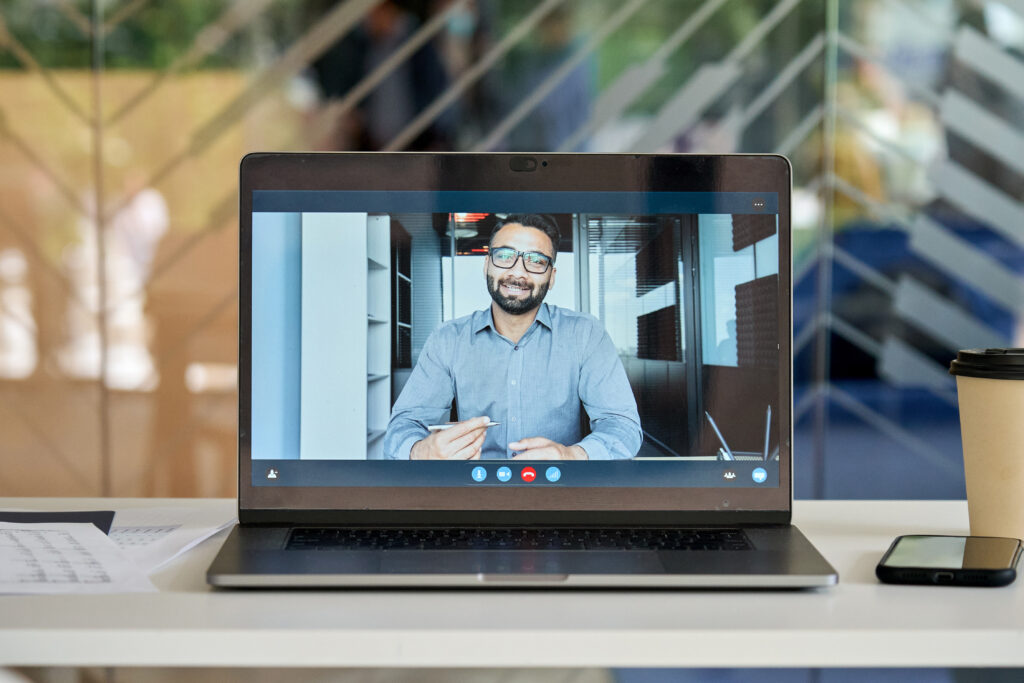 Laptop computer at office workplace table with smiling businessman executive leader, coach on pc screen having video chat, conference call, virtual meeting or giving training on videocall.